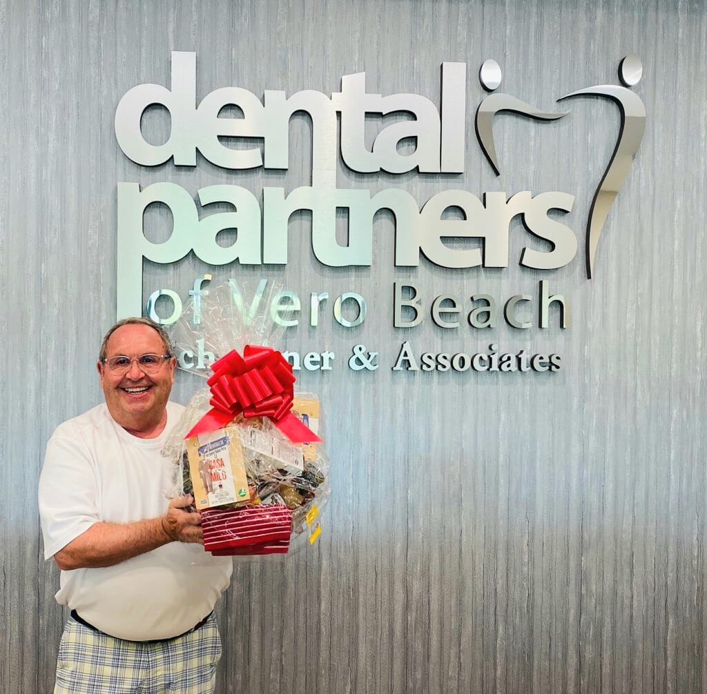 man standing in front of Dental Partners of Vero Beach holding gift basket