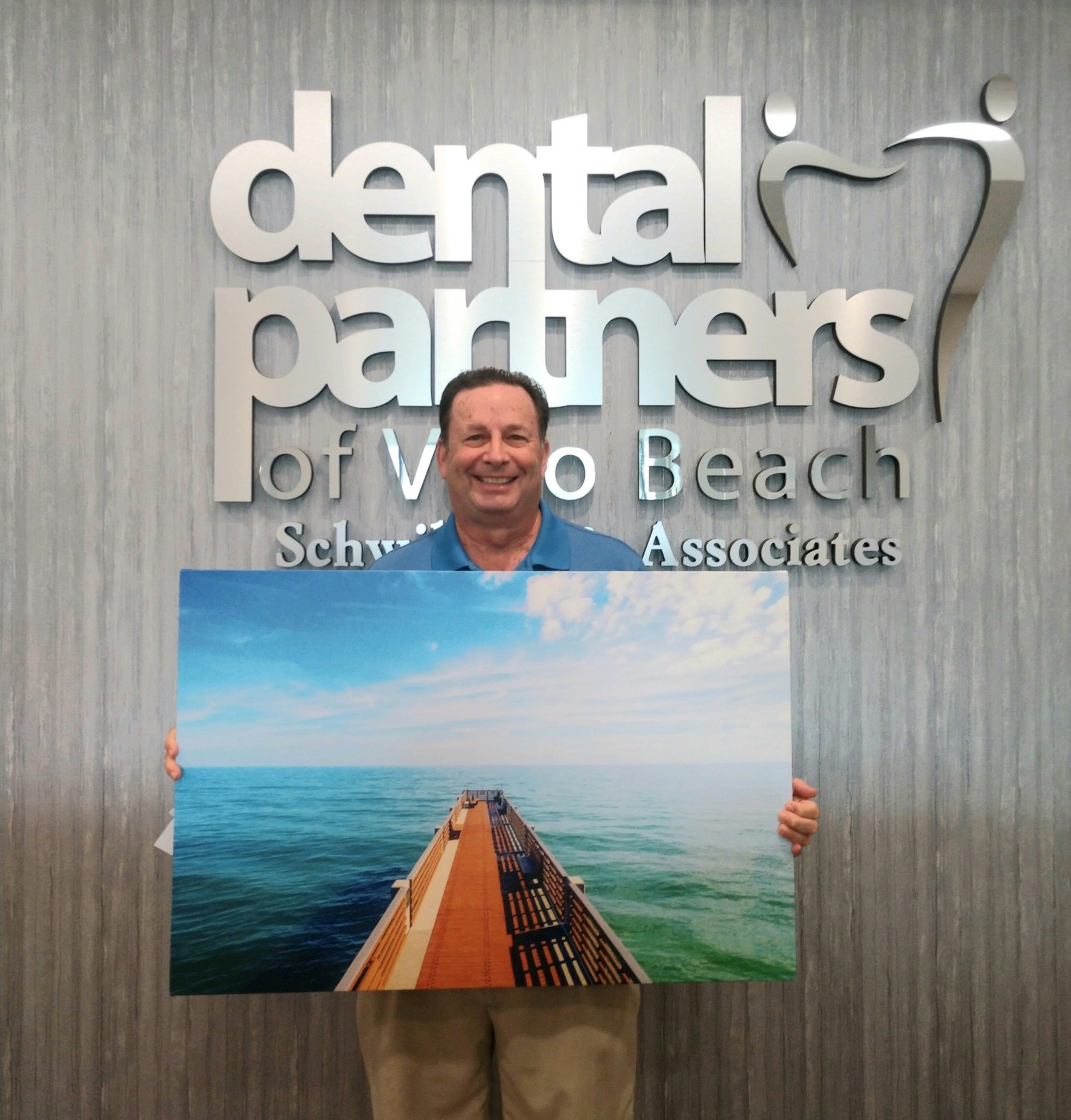 man standing in front of Dental Partners of Vero Beach holding large photo of dock